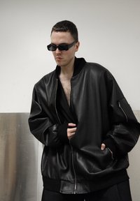 Veste bomber en cuir noir avec poignets et col côtelés, dotée d'une poche zippée sur la manche et d'une coupe décontractée.