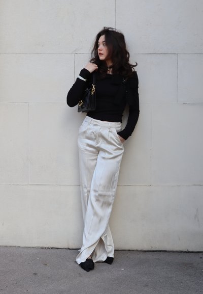 Pantalones de satén blanco con un corte relajado, combinados con una blusa negra de manga larga. El conjunto incluye un pequeño bolso negro con herrajes dorados.