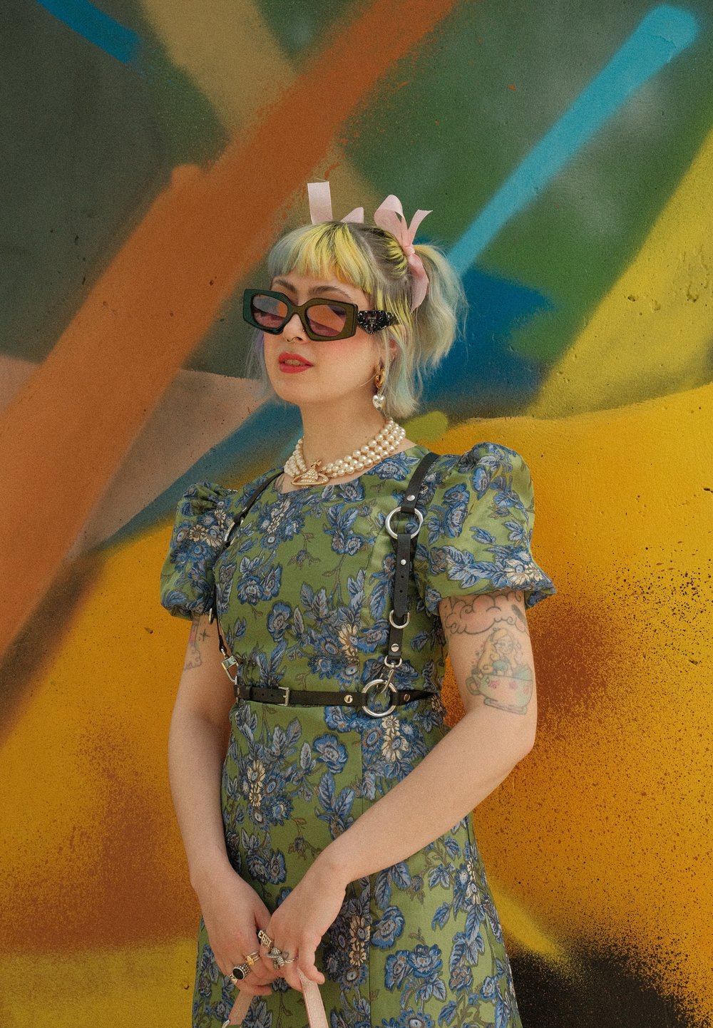 Φόρεμα πράσινου χρώματος με λουλούδια, με φουσκωτά μανίκια, μαύρος ιμάντας και ζώνη, στρωματοποιημένο κολιέ με πέρλες και μοναδικά, υπερμεγέθη γυαλιά ηλίου.