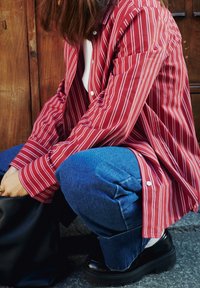 Camicia a righe rosse e bianche, vestibilità morbida con maniche lunghe, abbinata a pantaloni in denim blu e scarpe chunky nere. Borsa nera nelle vicinanze.