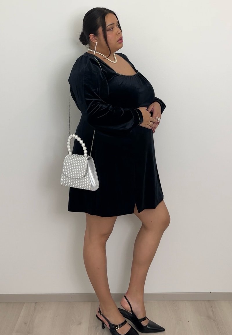 Black velvet long-sleeve dress with a deep neckline and side slit. Paired with a silver studded handbag and black slingback heels.