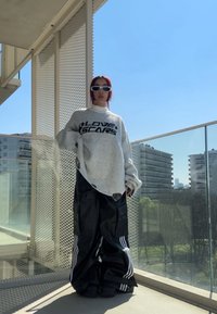 Suéter gris de gran tamaño con el texto "CICATRICES DE AMOR", acompañado de pantalones de cuero negro de pierna ancha con tres franjas blancas y roturas visibles.
