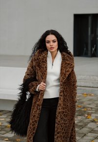 Pruun leopardimustriga mantel pehme tekstuuriga, kantud kreemja tõmbluku-svetari üle, koos mustade pükstega ja karvase musta kotiga.