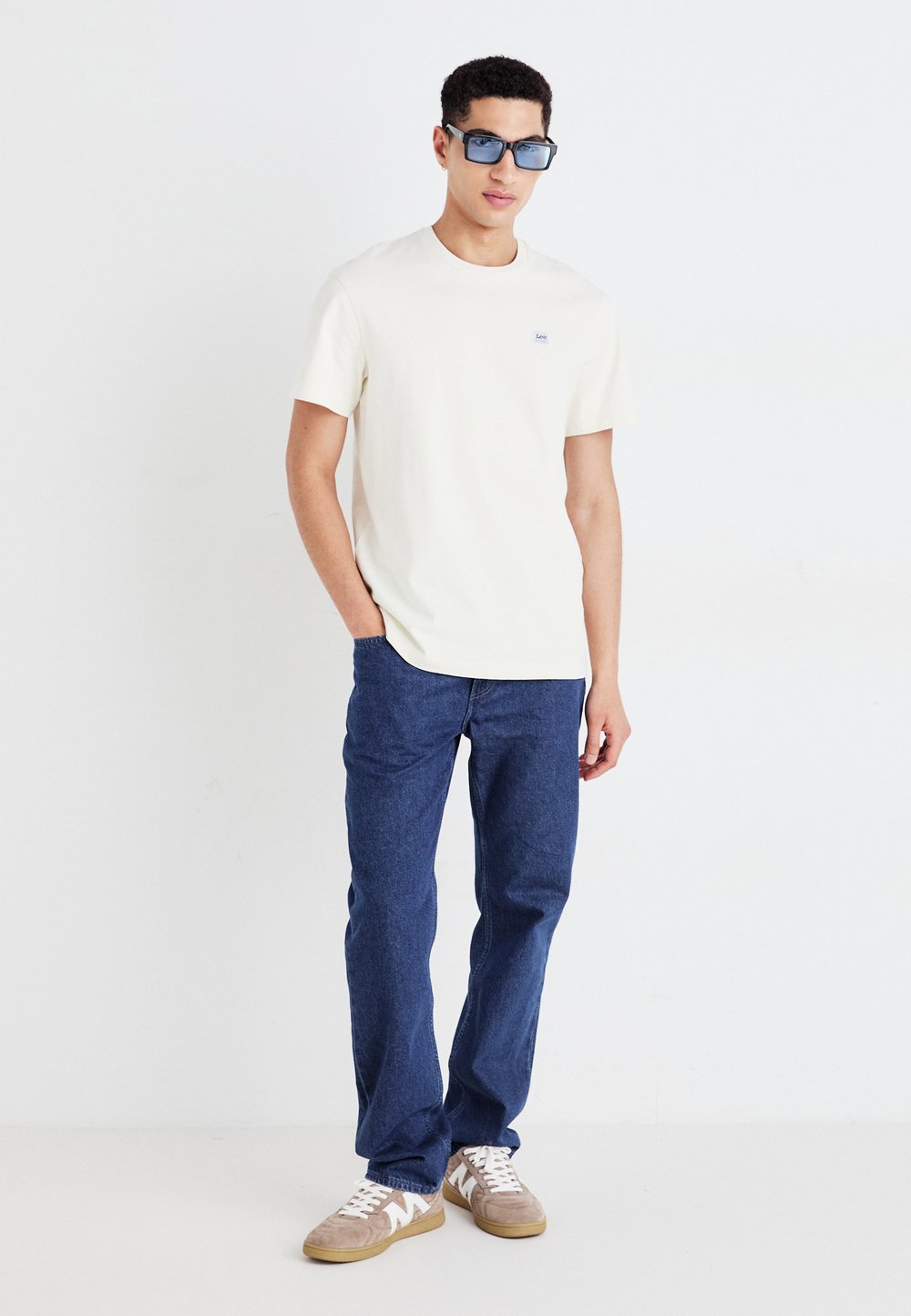 Ljusgrå bomullströja med en liten logotyp, i kombination med blå denimjeans och beiga sneakers med vita detaljer och runda snören.