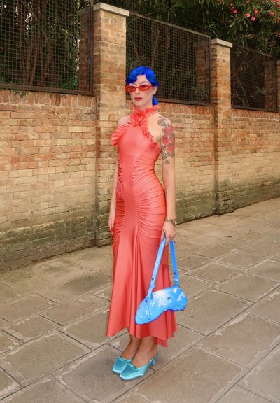 Vestido halter de color coral con detalles de volantes, diseño fruncido, combinado con un bolso de plástico azul y tacones cuadrados de color verde menta.