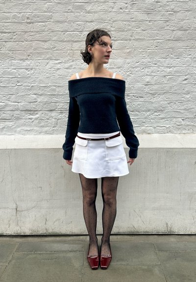 Jersey marino sin hombros, mini falda blanca con bolsillos, medias negras con lunares y tacones rojos de punta cuadrada. Diseño texturizado y en capas.