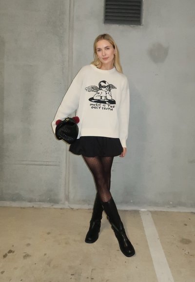 Sudadera blanca con un gráfico negro de una figura angélica y el texto "LA MÚSICA ES LA ÚNICA VERDAD". Combinada con una falda negra y botas hasta la rodilla.