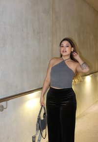 Top cropped cinza com nervuras e decote halter, combinado com calças largas de veludo pretas. O conjunto inclui uma bolsa cinza com alça de corrente.