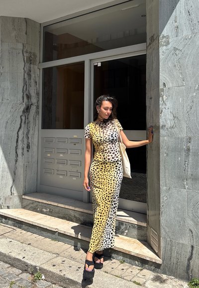 Vestido estampado con un degradado de amarillo y blanco con manchas de leopardo negras, combinado con sandalias de plataforma negras y un bolso de mano ligero.