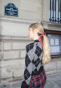 Black and grey argyle sweater with a fitted design, paired with a plaid skirt. Hair is long and styled with a red checkered ribbon.