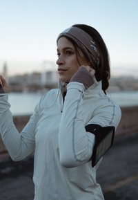 Femme en tenue de sport avec bandeau ajuste ses écouteurs, se préparant pour un exercice en plein air près de l'eau au crépuscule.