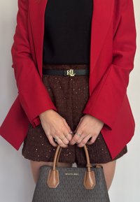 Rød blazer, sort top, brune teksturerede shorts med pailletter, sort bælte med guld "RL" spænde, og en grå Michael Kors taske med brune accentuer.