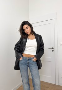 Black leather oversized blazer, white cropped tank top, light blue high-waisted jeans, featuring a smooth texture and minimalist design.