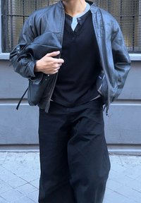Μαύρο δερμάτινο μπουφάν, γκρι πουκαμίσα henley και φαρδιά μαύρα παντελόνια; κρατώντας μία ταιριαστή μαύρη τσάντα. Υφή, χαλαρή εμφάνιση.