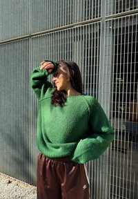 Grønn teksturert genser med løs passform, brukt sammen med brune joggebukser med elastisk midje og hvite striper. Mykt, koselig materiale, avslappet design.
