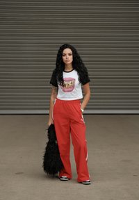 Hvit og svart grafisk T-skjorte med rosa munndesign, kombinert med røde joggebukser. Tilbehør inkluderer en svart teksturert håndveske og sneakers.