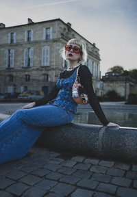 Jeansoutfit med en blå topp och utsvängda jeans, kombinerat med en svart transparent långärmad tröja. Accessoarer inkluderar stora solglasögon och en handväska.