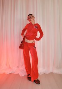 Survêtement en velours rouge avec logo "JUICY", accompagné de chaussons imprimés léopard noir et marron. Comprend un sac à main rouge assorti.