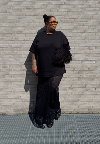 Camiseta negra de gran tamaño y falda negra de encaje con una textura transparente. Acentuada con una pieza de piel sintética negra y gafas de sol amarillas. Zapatos de plataforma negros.