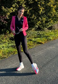 Roosa kerge jakk, must särk, mustad retuusid ja roosade aktsentidega tossud. Seisab teel, millel on rohelise taustaga.