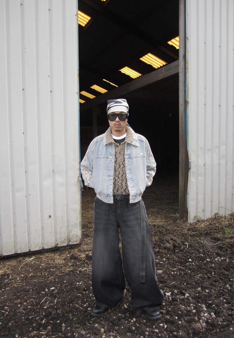 Veste en denim avec un col en fausse fourrure, pull à motifs, pantalon noir surdimensionné et grandes lunettes de soleil. Bandeau à rayures noires et blanches.