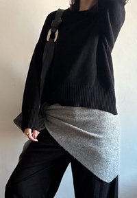 Pull noir surdimensionné avec ourlet côtelé, superposé à un tricot gris clair noué à la taille. Pantalon noir à jambes larges et sac avec un accent métallique.