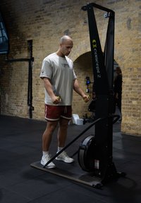 Concept2 romaskin i svart med et stort sentralt hjul. Brukeren holder grønne håndtak, iført en lys skjorte og røde shorts på et svart gulv.