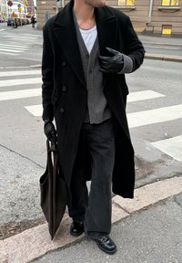 Dugi crni kaput, sivi kardigan, bijela košulja, tamne široke hlače, crne rukavice i cipele. Drži sivoprilagodljivu torbu.