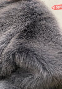 Fourrure synthétique gris foncé, texture dense et duveteuse, avec des longueurs de poils variées créant de la profondeur. Légère brillance et contours doux visibles.