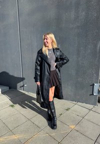 Sort læder trench coat over en grå striktrøje og en plisseret sort nederdel. Sorte knæhøje støvler og en lille sort taske fuldender looket.