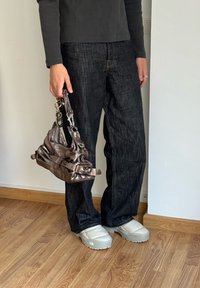 Black denim jeans with a relaxed fit, teamed with a crinkled brown handbag and light grey slip-on shoes. Smooth texture and minimal hardware.