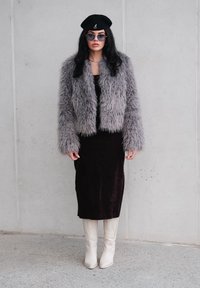 Szara kurtka z krótkim futerkiem z futra ekologicznego, dopasowana czarna sukienka i białe, szpiczaste kowbojki. Modelka ma na sobie czarny beret i okulary przeciwsłoneczne aviatory.