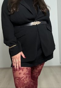 Blazer noir avec poches et ceinture feuille d'or, associé à des collants en dentelle bordeaux. Les mains aux ongles rouges ajoutent une touche d'élégance à la tenue.