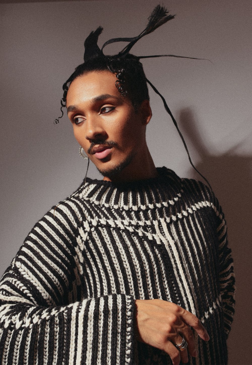 Pull en tricot à rayures noires et blanches avec un large décolleté et des manches évasées. Motif texturé notable et coupe ample. Les accessoires incluent des bagues.