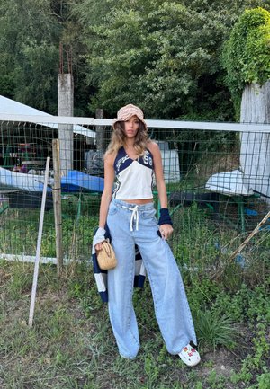 Jeans de pierna ancha de color azul claro combinados con un top recortado blanco y azul marino, llevando una bolsa de mimbre, y complementados con un sombrero tipo cubo color beige.