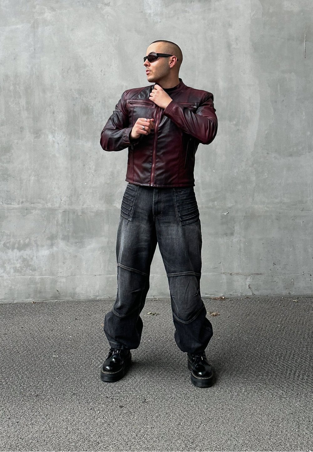 Giacca in pelle marrone con chiusura a zip, abbinata a pantaloni in denim scuri e comodi con dettagli testurizzati. Scarpe con tacco nero completano il look.