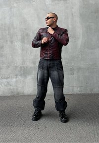 Giacca in pelle marrone con chiusura a zip, abbinata a pantaloni in denim scuri e comodi con dettagli testurizzati. Scarpe con tacco nero completano il look.