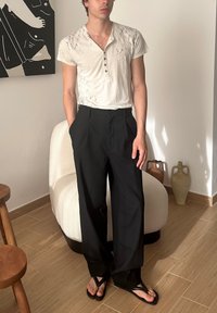 Vit kortärmad skjorta med marmordesign och knappar, tillsammans med svarta löst sittande byxor. Bärs med svarta flip-flops.