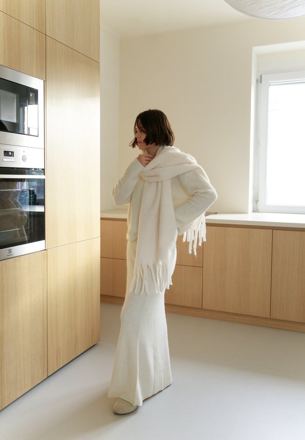 Witte gebreide trui en rok set met franjes, aangevuld met een bijpassende sjaal, in een moderne keuken met houten kasten.