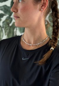 Juoda Nike sportinė marškinėliai trumpomis rankovėmis su mažu pilku logotipu. Sluoksniuotos vėriniai su karoliukais ir auksiniais akcentais, taip pat pintos plaukų detalės.