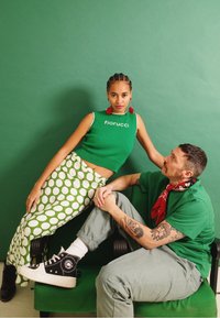 Top crop verde com o logótipo "Fiorucci", saia verde com bolinhas, sapatilhas de cano alto pretas e acessórios, contra um fundo verde.