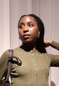 Oliwkowo zielona, prążkowana bluzka z długim rękawem, z dekoltem typu henley i sześcioma guzikami; prezentowana torebka na ramię z eleganckim, ciemnym paskiem i ozdobami z metalu.