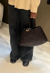 Vevd mørkebrun håndveske med dobbelthåndtak, med et teksturert mønster og små anheng. Kombinert med svarte vide jeans og sko.