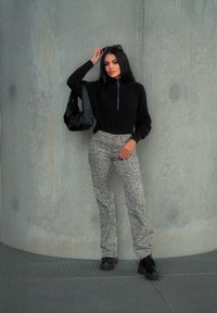 Μαύρο ζακέτα με φερμουάρ και ριμπ υφή, συνδυασμένη με γκρι παντελόνι με animal print και μαύρες μπότες με κορδόνια. Μαύρη τσάντα στον ώμο.