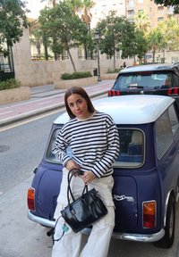 Camisa de manga longa riscada, bege e preta, combinada com calças cargo bege; bolsa preta com detalhes em prata. Fundo com carro vintage roxo.