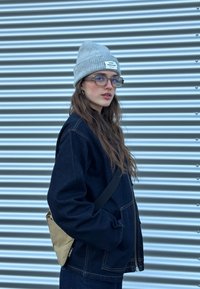 Τζάκετ τζιν σε σκούρο μπλε με φερμουάρ, συνδυασμένο με γκρι πλεκτό σκουφάκι. Οι διαφάνειες και μία μικρή χρυσή τσάντα συμπληρώνουν την εμφάνιση.