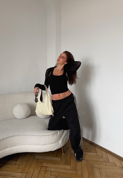 Top corto negro y pantalones deportivos negros oversize con rayas blancas en los laterales; sostiene un bolso de hombro color crema y gafas de sol negras.
