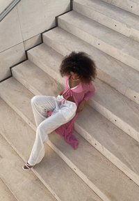 Rosa texturerad omlottopp över en vit lös passform, sittande på ljusa stentrappor i en modern arkitektonisk miljö.