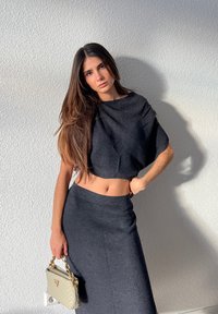 Črn rebrast crop top v kombinaciji z dolgim krilom, ki ima oprijet silhueto. Obleko dopolnjuje svetla torbica s verižnim trakom.