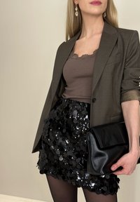 Top marrón con canalé, blazer gris, minifalda negra de lentejuelas, bolso de mano negro. Combinado con medias negras transparentes y pendientes de araña.